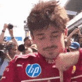 a man with a mustache is standing in front of a crowd wearing a red hp shirt .