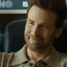 a man with a beard is smiling and sitting in a chair .
