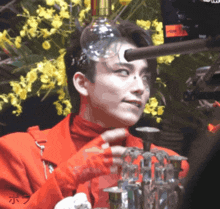 a man in a red jacket is holding a bottle of water on his head