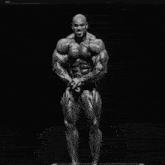 a black and white photo of a bodybuilder flexing his muscles in front of a black background .