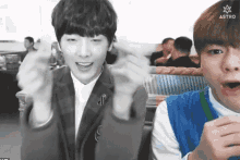 two young men are sitting next to each other in a restaurant and one of them is wearing a blue vest .