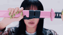 a woman with green nails is holding a pink samurai sword in front of her eyes .