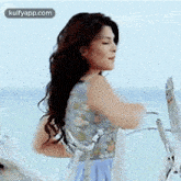 a woman in a blue dress is standing on a beach with a rope around her waist .