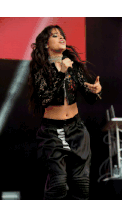 a woman singing into a microphone while wearing a black crop top and black pants