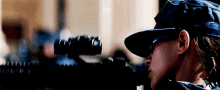 a woman wearing a hat and sunglasses is holding a rifle