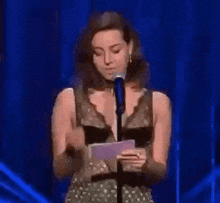 a woman is holding a piece of paper in front of a microphone and crying .