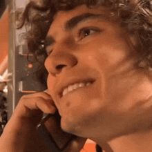 a man with curly hair is smiling while talking on a cell phone