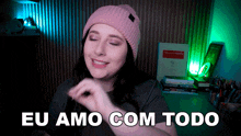 a woman wearing a pink beanie and a grey shirt says eu amo com todo