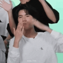 a young man in a white sweater is blowing a kiss .