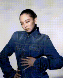 a woman in a denim shirt is standing with her hands on her hips and looking at the camera .