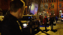 a group of people walking down a street at night with an ambulance behind them