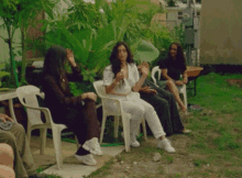 a group of women are sitting in plastic chairs in a yard
