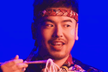 a man wearing a headband is eating noodles from chopsticks