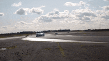 a white car is driving on a road with a cloudy sky in the background