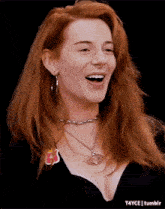 a woman with red hair is wearing a choker and earrings and smiling .