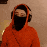 a man wearing an orange hoodie and headphones is covering his face with a black mask .