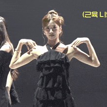 a woman in a black dress is flexing her muscles in front of a yellow sign that says lg
