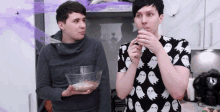 two men are standing next to each other in a kitchen . one of the men is wearing a ghost shirt .
