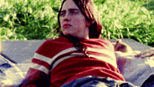 a young man in a red and white striped shirt is laying on a couch in the grass .