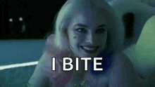 harley quinn from suicide squad is smiling and says `` i bite '' while sitting in a bathtub .