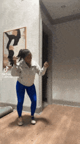 a woman in blue leggings is dancing in a hallway with a picture on the wall behind her that says tik tok