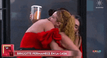 a woman in a red dress is hugging another woman in front of a sign that says briggitte permanece en la casa