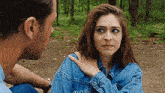 a man is putting his hand on a woman 's shoulder while they are sitting in the woods .