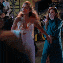 a woman in a white strapless dress stands next to another woman in a blue coat