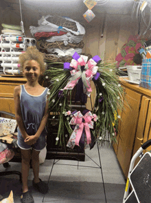 a little girl stands in front of a wreath with a pink and purple bow