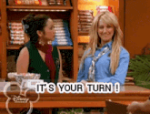 two women are standing next to each other in a store and the words it 's your turn are on the screen