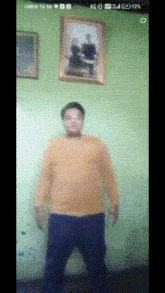 a man in a yellow shirt is standing in front of a green wall ..