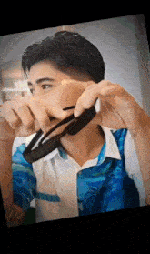 a young man wearing a blue shirt is holding a pair of sunglasses in his hand .