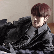 a young man with red hair is laying on a bed wearing a black jacket that says titan on it
