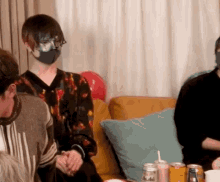 a man wearing a mask is sitting on a couch with a group of people .