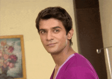 a man in a purple shirt stands in front of a framed picture of flowers