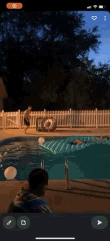 a phone screen shows a man standing next to a swimming pool at night