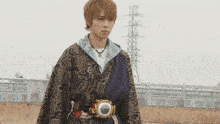a young man wearing a kimono and a belt with a camera on it stands in a field