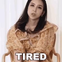a woman in a floral dress sits in a chair with the word tired above her head