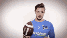 a man in a blue shirt with the number 5 on it holds a football