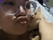 a woman wearing glasses kisses an orange cat on the cheek