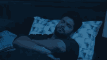 a man with a beard is laying in bed with a blue light shining on his face .