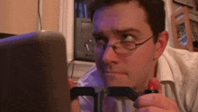 a man wearing glasses is holding a steering wheel in front of a laptop computer .