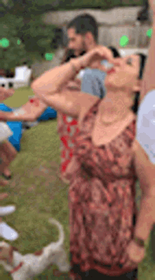 a woman in a red dress is drinking from a bottle while a dog looks on .