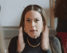 a woman wearing a black turtleneck and gold earrings is making a funny face .