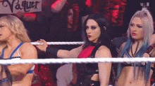 three women are standing in a wrestling ring with a sign that says vaquer on it