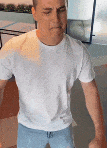 a man in a white t-shirt and blue jeans is making a funny face