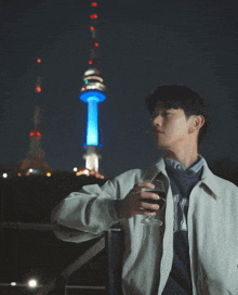 a man holding a glass of wine in front of a tower with a blue light on it