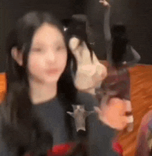 a girl with long black hair is sitting at a table holding a bottle of wine and looking at the camera .
