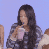 a woman in a striped shirt is drinking a pink drink with a blue straw .