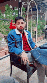 a man wearing a denim jacket and a red shirt is sitting in a chair with tiktok written on the bottom right